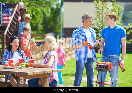 Portrait de jeunes hommes saucisses à frire et parler à la campagne à week-end avec leurs familles près de par Banque D'Images