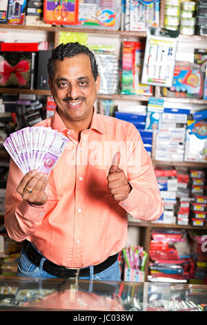 1 Indian shop keeper man showing Thumbs up avec de l'argent en espèces en magasin stationnaire Banque D'Images