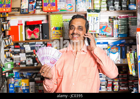 1 Indian shop keeper homme montrant l'argent parle de roupies et téléphone dans l'arrêt shop Banque D'Images