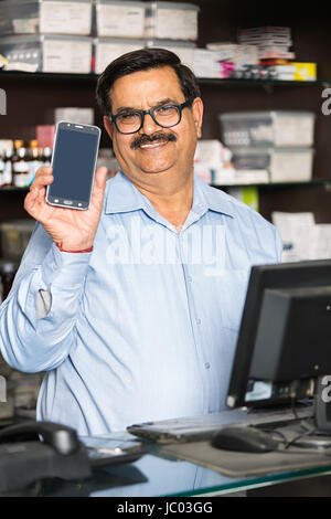 1 Indian shop keeper man nouveau téléphone mobile en pharmacie store keeper Banque D'Images