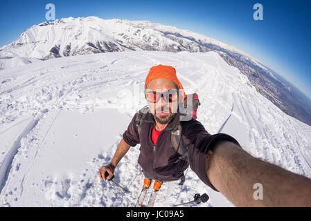 Skieur alpin adultes avec barbe, lunettes de soleil et chapeau, en tenant sur selfies pente enneigée dans les Alpes italiennes avec beau ciel bleu clair. Image tonique, vintage Banque D'Images