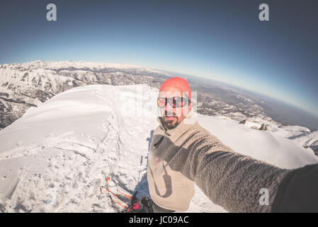 Skieur alpin adultes avec barbe, lunettes de soleil et chapeau, en tenant sur selfies pente enneigée dans les Alpes italiennes avec beau ciel bleu clair. Image tonique, vintage Banque D'Images