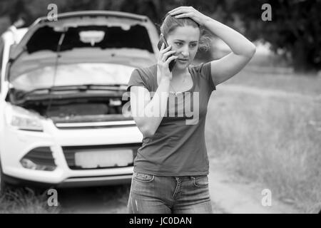 Portrait noir et blanc de sad woman standing at broken voiture et appelant à l'aide Banque D'Images