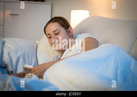 Portrait of beautiful smiling woman reading on digital tablet au lit avant de dormir Banque D'Images