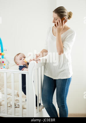 Portrait de jeune femme qui travaille à la maison et parler au téléphone tout en alimentant son bébé Banque D'Images