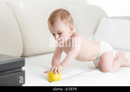 Adorable baby boy crawling on lit et atteindre pour apple Banque D'Images