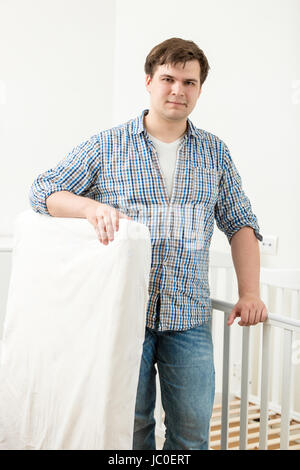 Portrait of young handsome man posing à lit bébé avec matelas neuf Banque D'Images