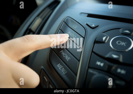 Photo Gros plan femme de doigt qui appuie sur le bouton radio situé à panneau de voiture Banque D'Images