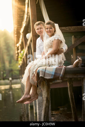 Heureux couple nouvellement marié assis sur la vieille jetée en bois de Banque D'Images