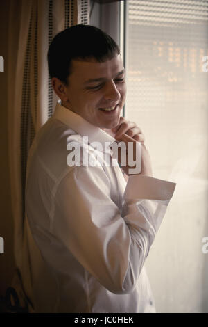 Tonique portrait of smiling homme élégant à mettre sur la chemise blanche de la fenêtre Banque D'Images