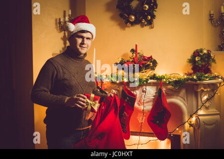 Photo aux couleurs de young smiling man taking boîte-cadeau hors du sac rouge Santa Banque D'Images