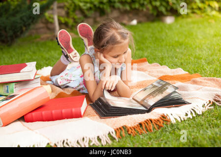 Petite fille mignonne en tenue d'altitude sur l'herbe et regarder des photos Banque D'Images