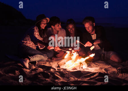 Amis assis sur la plage près de clink glasses bonfire Banque D'Images