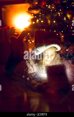 Portrait of cute girl couché sous l'arbre de Noël et à la pétillante en boîte-cadeau Banque D'Images