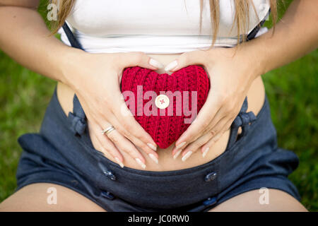 Photo gros plan de pregnant woman holding red heart tricoté à l'estomac Banque D'Images