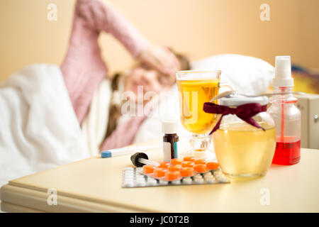 Pot de miel, tasse de thé et des médicaments se trouvant sur la table à côté du lit de fille malade Banque D'Images