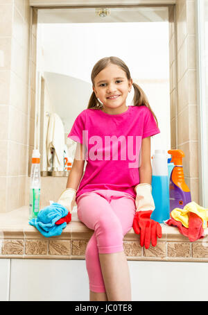 Portrait of smiling girl sitting on évier salle de bains au nettoyage tout en faisant Banque D'Images