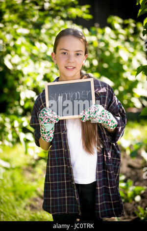 Smiling brunette girl holding tableau avec word 'Summer' au jardin Banque D'Images