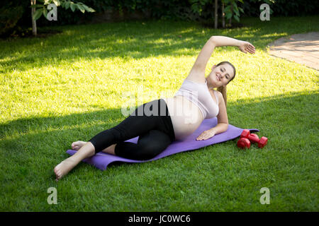 Les jeunes femmes enceintes yoga étirements avant sur l'herbe au parc Banque D'Images