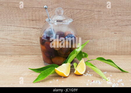 Un bol en verre avec des olives à l'huile d'olive sur un fond de bois avec citron, sel de mer. La cuisine grecque traditionnelle. Banque D'Images