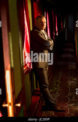 Beau jeune homme en costume gris posant en vieux train Banque D'Images