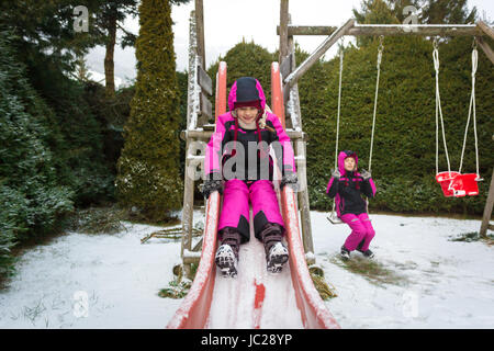 Deux professionnels de petites filles s'amuser sur l'aire de jeux au jour de neige froide Banque D'Images