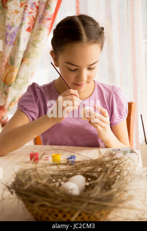 Portrait de concentrés girl painting Easter eggs at table Banque D'Images