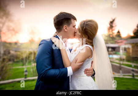 Portrait de l'élégant couple nouvellement marié kissing in park au coucher du soleil Banque D'Images