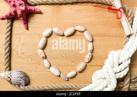 Cœur fait de coquillages avec bordure de cordes et de noeuds sur fond de bois Banque D'Images