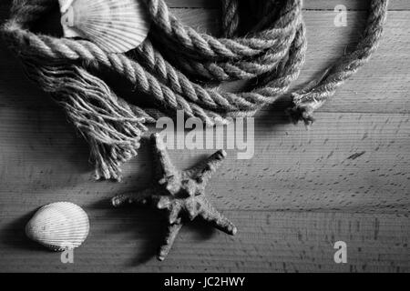 Gros plan noir et blanc photo de vieille corde et coquillages couchée sur un bureau en bois Banque D'Images