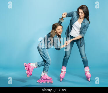 Mère et fille en patins à s'amuser en studio sur bleu Banque D'Images