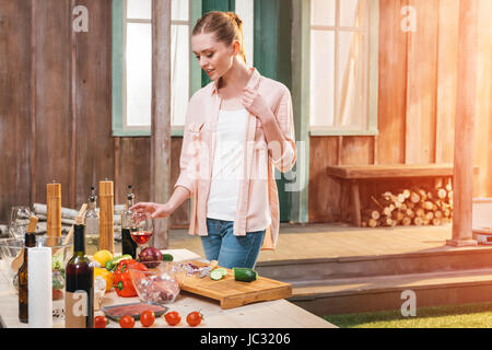 Jeune femme tenant un verre de vin à table avec la viande et les légumes à l'extérieur Banque D'Images