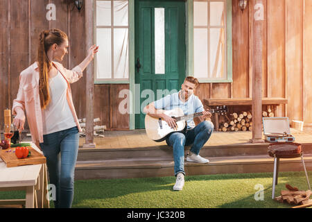 L'homme et la femme se reposant sur le porche, l'homme jouant à la guitare Banque D'Images