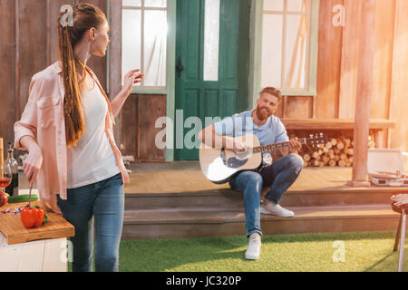 L'homme et la femme se reposant sur le porche, l'homme jouant à la guitare Banque D'Images