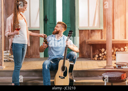 L'homme et la femme se reposant sur le porche, l'homme jouant à la guitare Banque D'Images