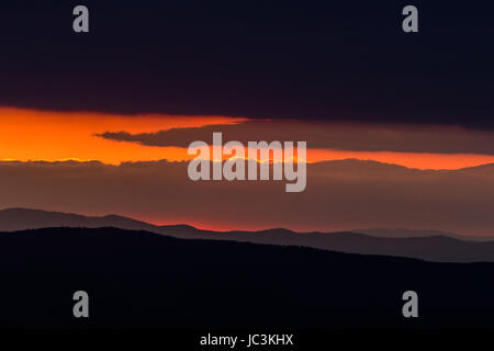 Un coucher de soleil entre certains pans de montagnes et nuages sombres, créant une bande oblique Banque D'Images