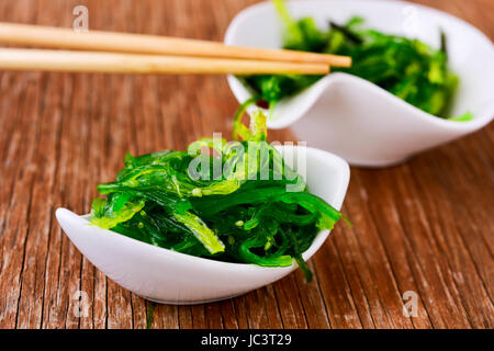 Salade d'algues wakame goma ou dans certains bols de céramique blanc, sur une table en bois rustique Banque D'Images