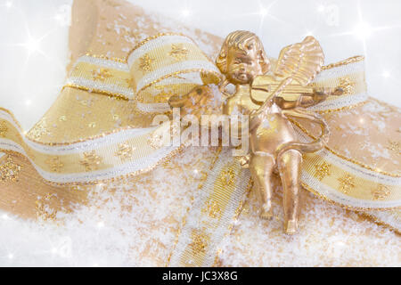 Close up of golden présente fort avec angel à jouer du violon pour Noël sur fond de neige Banque D'Images