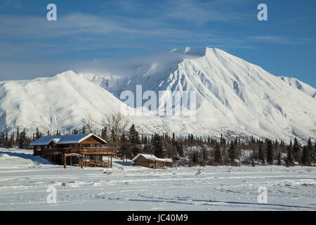 Des cabanes en Alaska s'asseoir à la base d'un lac gelé avec les montagnes enneigées en arrière-plan. Banque D'Images