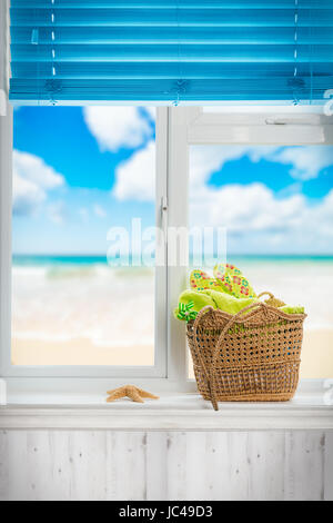 Panier de plage rempli de serviette et des tongs dans la fenêtre Banque D'Images