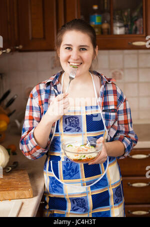 Beautiful smiling Ménagère cuisine manger sur salade Banque D'Images