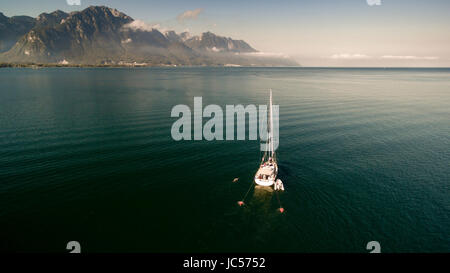 Bateau à voile ancré dans le lac de Genève dans le Canton de Vaud sur une belle journée avec des montagnes en arrière-plan et de ciel bleu. Banque D'Images