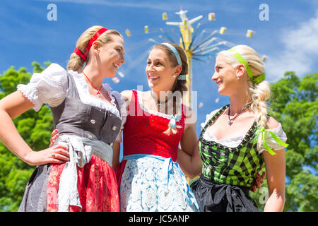 Les femmes amis visitant festival folklorique bavarois Dirndl en face de carrousel Banque D'Images