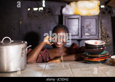 Une femme chef dans sa cuisine avec des casseroles et des poêles, tenant son téléphone portable. Nigeria, Afrique Banque D'Images