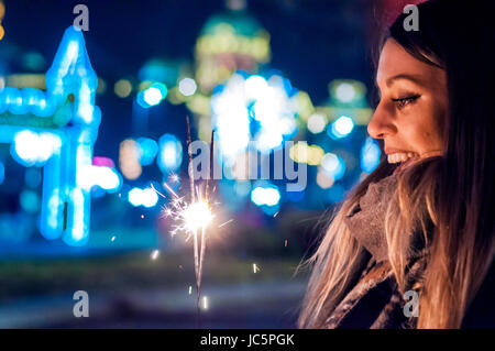 Belle Jeune femme debout et tenant des cierges merveilleux sur fond brillant. Woman holding sparkler dans sa main, célébrant le Nouvel An Banque D'Images