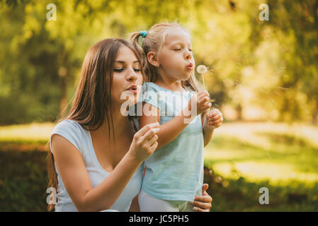 Happy cute little girl blowing dandelion avec mère dans le parc. Banque D'Images