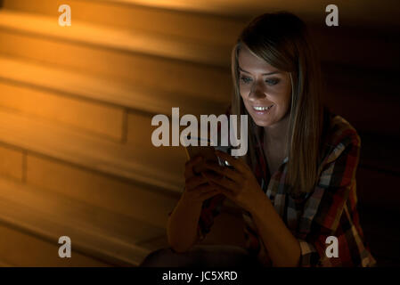 Young beautiful business woman sitting at night lights avec téléphone intelligent. Soirée femme travaillant à distance. Surf cours internet, reading book Banque D'Images