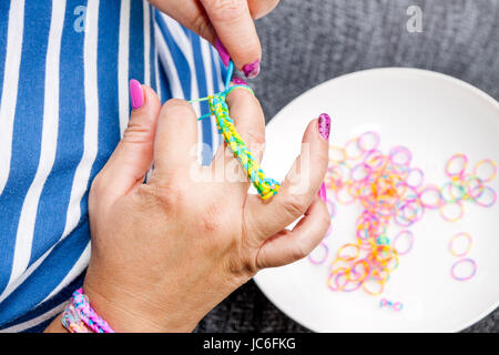 Les femmes avec des ongles colorés faisant une gaine de caoutchouc bracelet avec un crochet . Mains de près. Les jeunes nouveau concept de mode moderne. Banque D'Images