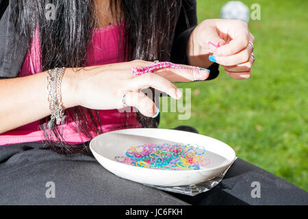 Fille aux ongles colorés faisant une gaine de caoutchouc bracelet avec un crochet . Mains de près. Les jeunes nouveau concept de mode moderne. Banque D'Images