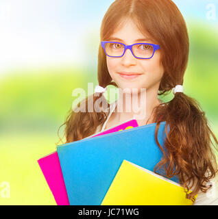 Closeup portrait of cute heureux lycéenne en plein air, portant des lunettes, tenant dans les mains, de l'éducation dossiers colorés différents concept Banque D'Images